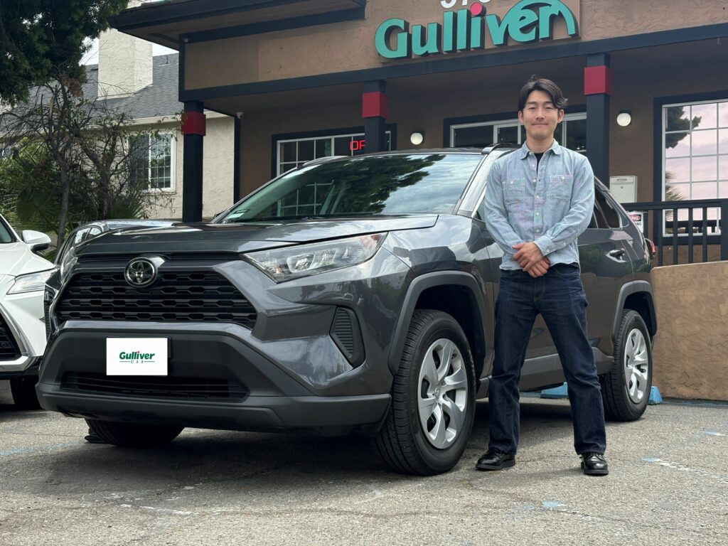 Man standing beside a gray SUV in front of a Gulliver dealership storefront.